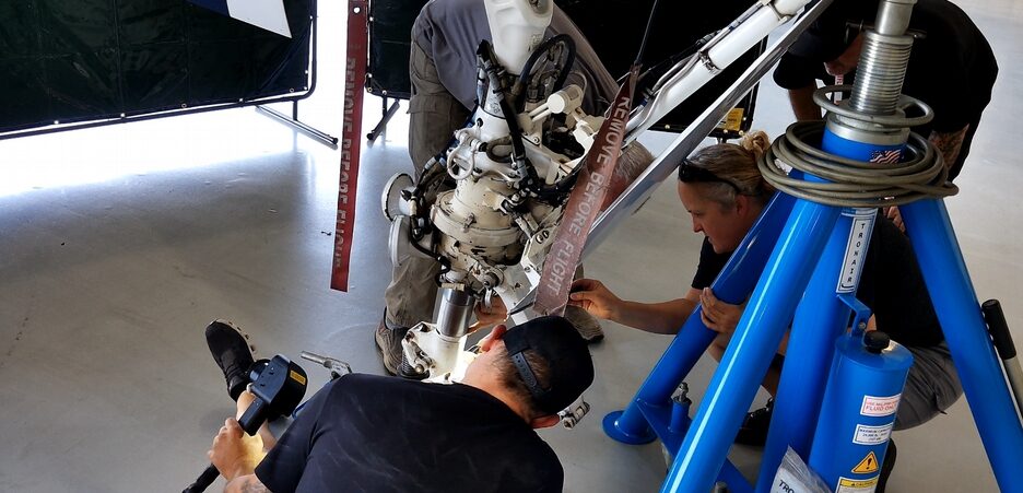 A technician aiming a non-contact infrared thermometer at a landing gear strut while two others work on the assembly.